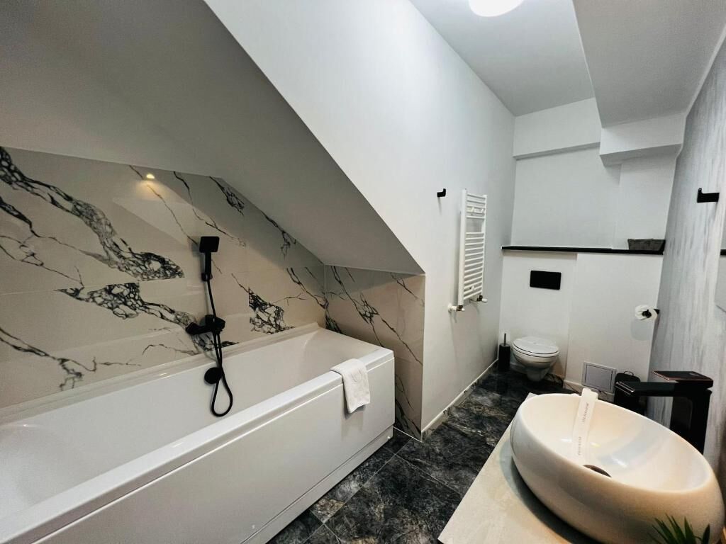 A modern bathroom with a marble wall, a bathtub, a toilet, and a sink.