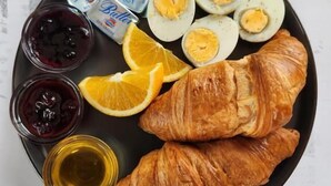 Un plato con huevos, croissants, gajos de naranja y salsas.