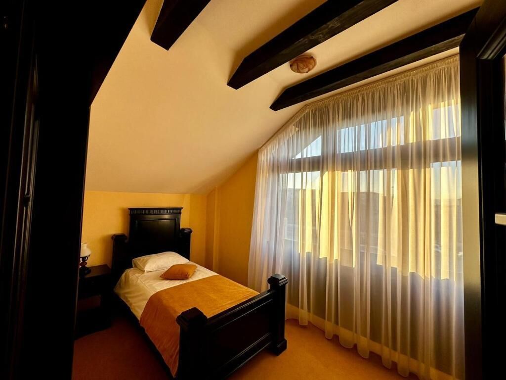 Un dormitorio con cama, mesita de noche, cabecera de madera y ventana con cortinas traslúcidas.