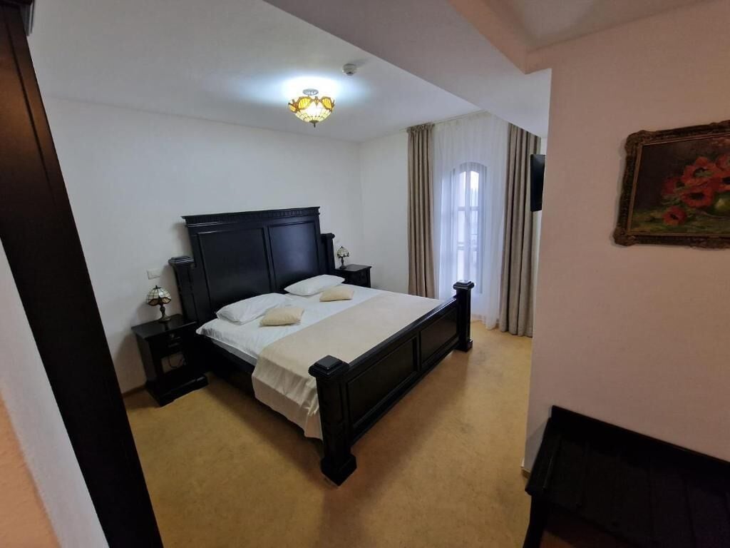 A bedroom with a large bed, a nightstand, a lamp, and a painting on the wall.