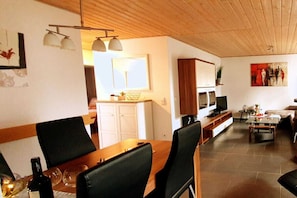 Un salon moderne avec une table à manger en bois, des chaises noires, un téléviseur et un canapé.