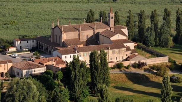 Un grand bâtiment historique, doté de plusieurs ailes, entouré d’une végétation luxuriante et situé dans un paysage vallonné.