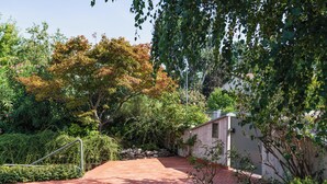 Une terrasse dallée, agrémentée d’une rambarde en métal, entourée d’une végétation luxuriante et d’arbres.