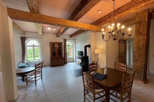 Enjoy a serene atmosphere in this spacious room with a high ceiling, dining table, and large window offering a view of lush greenery.