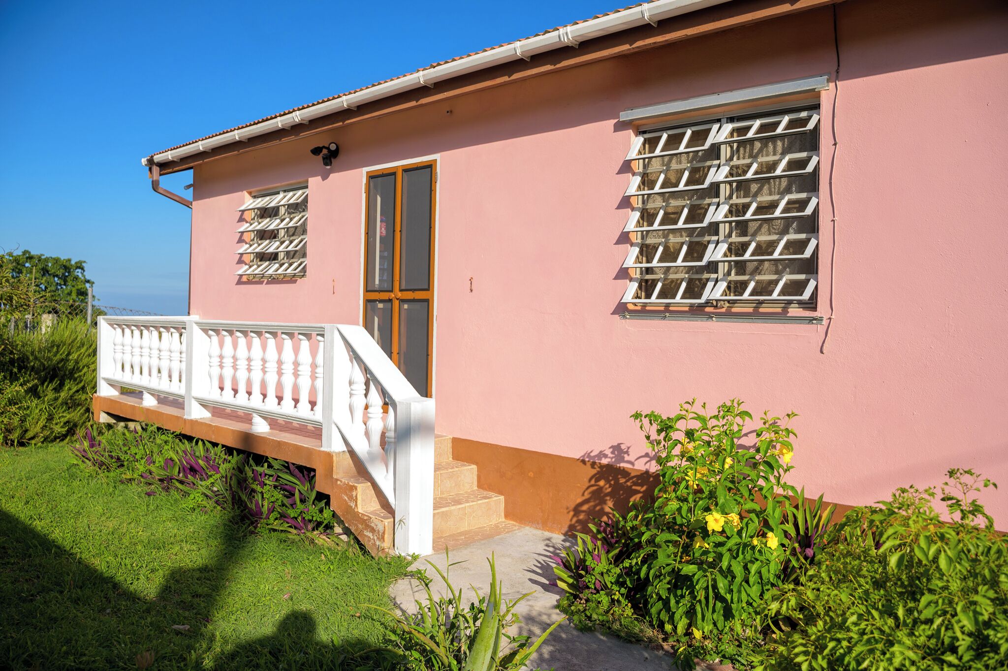 A pink building with a white railing, a door, and two windows with shutters.