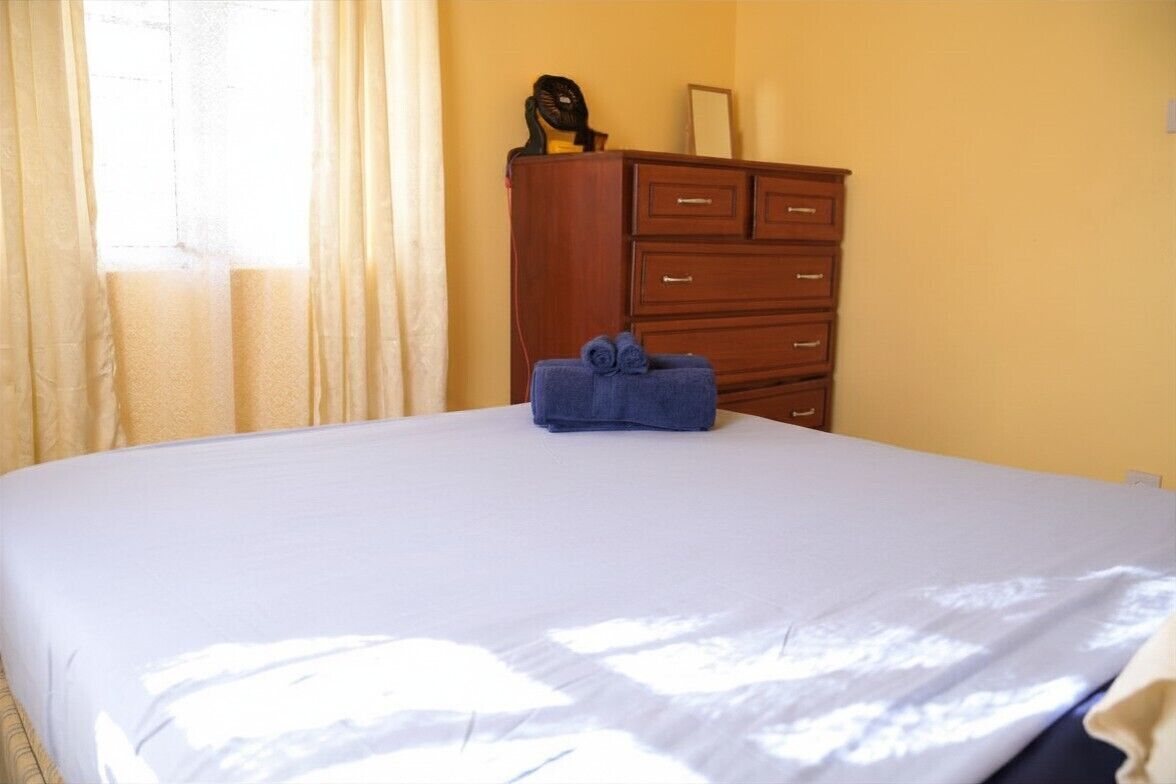 A hotel room with a bed, a wooden dresser, and a window with curtains.