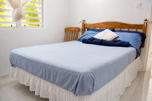 A bed with a wooden headboard, a white skirted bed skirt, and a blue bedspread.