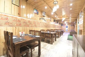 A restaurant with wooden walls, multiple tables, and chairs. - Hotel Grand Majestic (Jaipur)