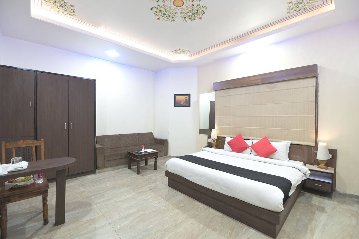 Una habitación de hotel con cama, escritorio, sofá, armario e iluminación decorativa en el techo.