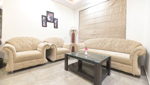 A living room with two beige sofas, a glass coffee table, and a patterned wall. - Hotel The Grand Majestic (Jaipur)