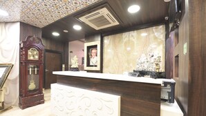 A reception desk with a marble backdrop, a clock, and a framed portrait. - Hotel The Grand Majestic (Jaipur)