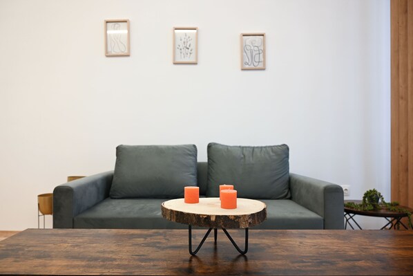 A modern living room with a grey sofa, two orange candles on a wooden round table, and three framed artworks on the wall.