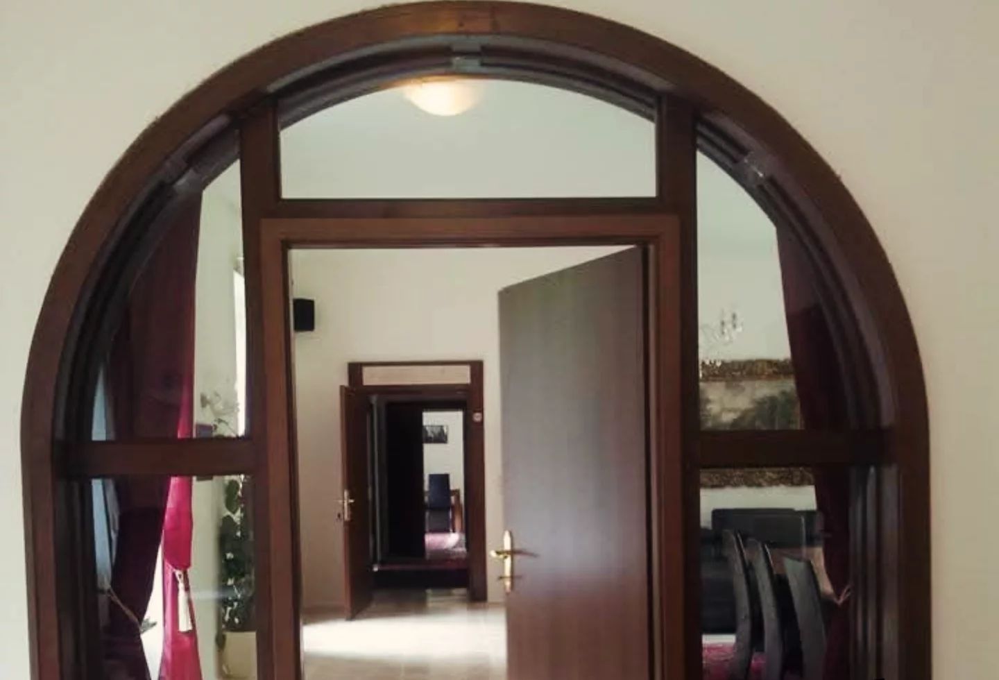 An arched doorway leading into a hallway with a tiled floor and a view of a room with a bed and a window.