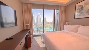 Habitación de hotel con una cama grande, un escritorio, televisión y balcón con vista a la ciudad.