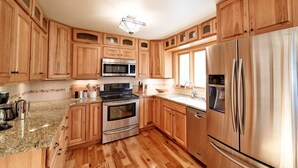 A modern kitchen with wooden cabinets, stainless steel appliances, granite countertops, and a wooden floor. - Spacious Sunny Home with 3 bedrooms, 2 bathrooms, a Big Fenced Yard near Downtown, near walking paths, bridge over creek, park, pool, playgrounds, splash area, YMCA and historic downtown Sheridan all within walking distance. (Sheridan)