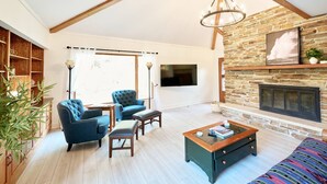 A spacious living room with a high ceiling, a stone fireplace, and a large window. - Spacious Sunny Home with 3 bedrooms, 2 bathrooms, a Big Fenced Yard near Downtown, near walking paths, bridge over creek, park, pool, playgrounds, splash area, YMCA and historic downtown Sheridan all within walking distance. (Sheridan)