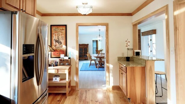 A modern kitchen with wooden cabinets, a stainless steel refrigerator, and a dining area with a blue rug. - Spacious Sunny Home with 3 bedrooms, 2 bathrooms, a Big Fenced Yard near Downtown, near walking paths, bridge over creek, park, pool, playgrounds, splash area, YMCA and historic downtown Sheridan all within walking distance. (Sheridan)