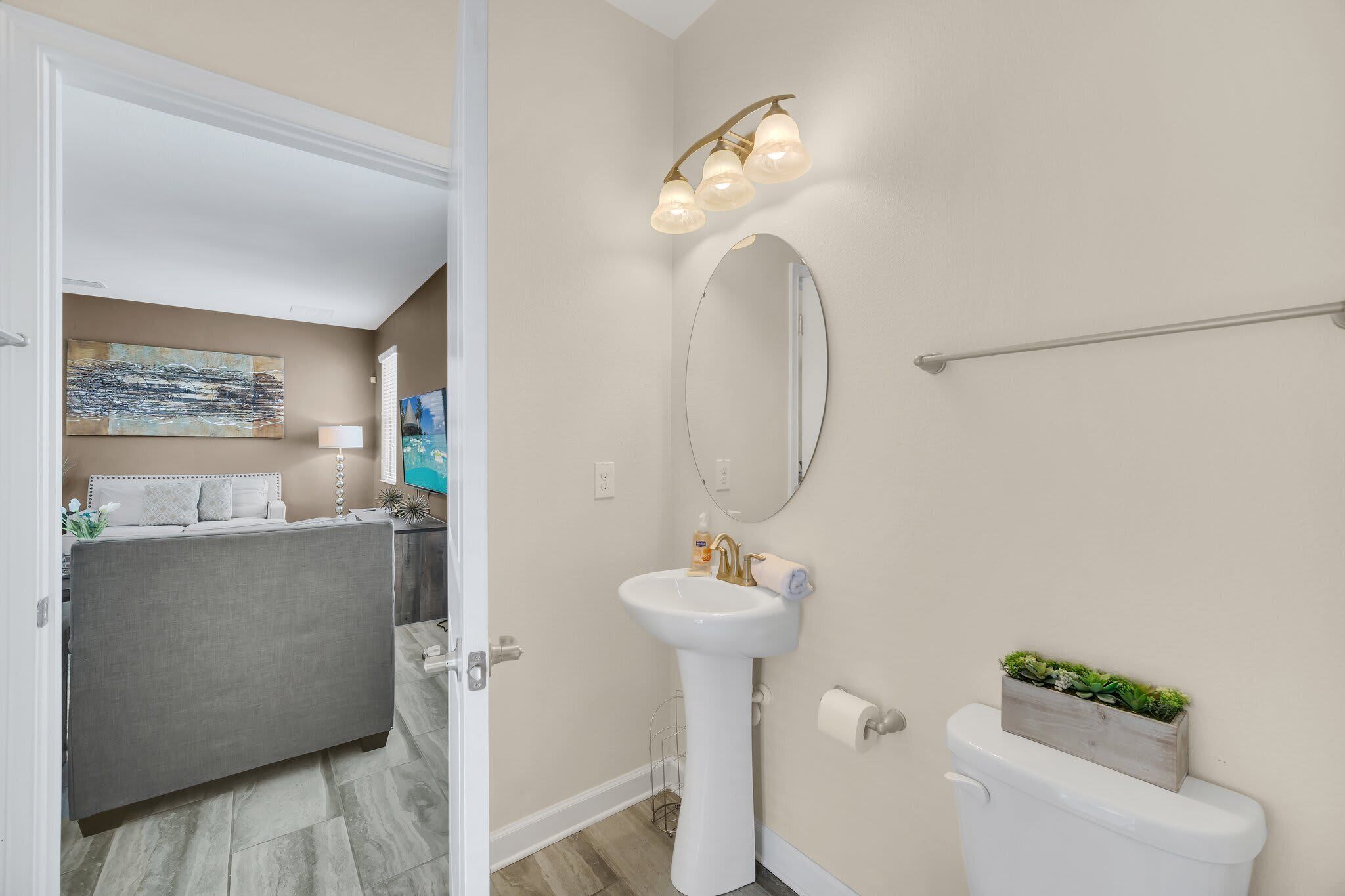 A bathroom with a white sink, a mirror, and a toilet. There is a towel rack above the sink and a small plant on the toilet.