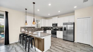 A modern kitchen with white cabinets, a stainless steel refrigerator, and a central island with bar stools.