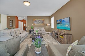 A living room with a sofa, coffee table, and TV. There is a painting on the wall and a plant on the coffee table. - Private Pool & Spa | Lazy River | Near Disney 1517 (Four Corners)