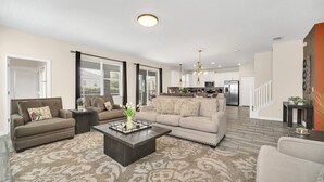 A spacious living room with a large sofa, a coffee table, and a kitchen in the background.