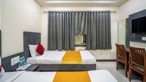Ein Hotelzimmer mit zwei Betten, einem Schreibtisch, einem Stuhl, einem Fernseher und einem Fenster mit Vorhängen.