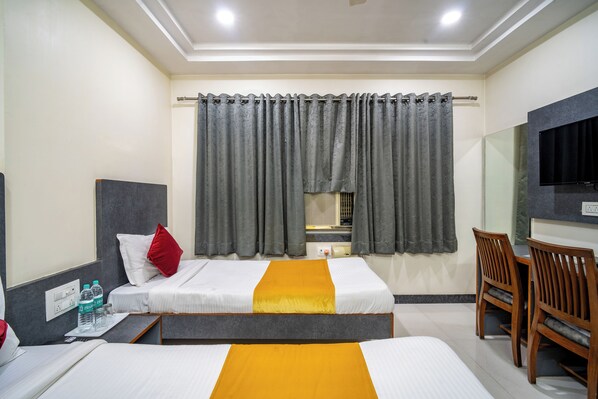 A hotel room with two beds, a desk, a chair, a TV, and a window with curtains. - Hotel Ville Parle (Luni)