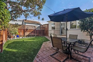 Une terrasse avec une table et des chaises, un parasol bleu et une pelouse bien entretenue.