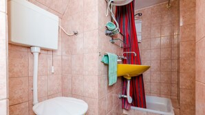 Une salle de bain avec des toilettes jaunes, un lavabo blanc, un rideau de douche rouge et une baignoire blanche.