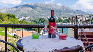 Une table avec une bouteille de vin et des verres, placée sur un balcon donnant sur un paysage montagneux.