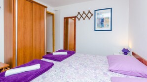 Une chambre à coucher avec un lit, deux serviettes violettes, une armoire en bois, un tableau encadré et une table de chevet avec une lampe.
