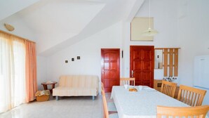 Ein geräumiges Zimmer mit Esstisch, Holzsesseln, einer Couch und einem kleinen Tisch mit einem Korb.