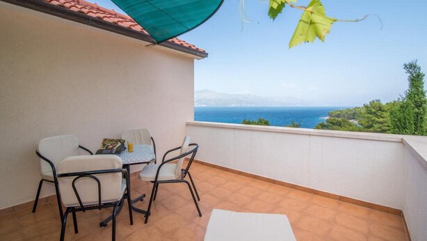 Ein Balkon mit Tisch, Stühlen und einem grünen Sonnenschirm, mit Blick aufs Meer.