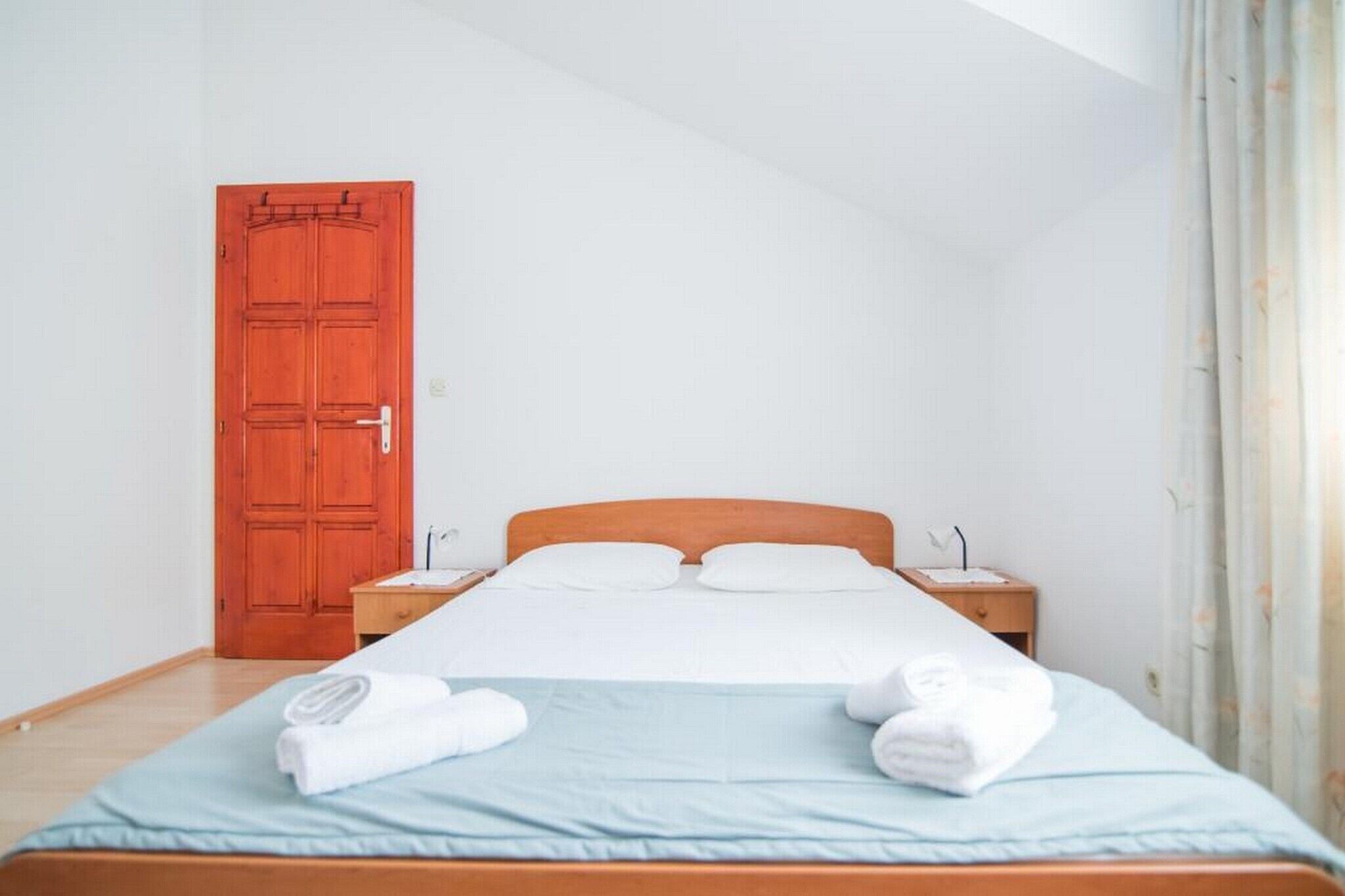 Habitación de hotel con una cama individual, cabecera de madera, dos mesitas de noche y una puerta roja.