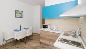A compact kitchen with a microwave, kettle, and sink. There is a dining table with chairs and a painting on the wall. - Apartments Marmo - Superior One Bedroom Apartment with Balcony and Sea View (Apartman 3) (Mlini)