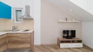 A modern kitchen with a built-in stove, a microwave, and a sink. There is a wooden cabinet with drawers and a countertop with a kettle. A television is placed on a wooden stand against the wall. - Apartments Marmo - Superior One Bedroom Apartment with Balcony and Sea View (Apartman 3) (Mlini)