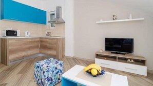 A modern kitchen with wooden cabinets, a microwave, and a television. There is a small table with a fruit bowl and a colorful ottoman. - Apartments Marmo - Superior One Bedroom Apartment with Balcony and Sea View (Apartman 3) (Mlini)