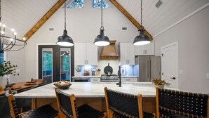 Une cuisine dotée d’un îlot en marbre, de chaises en bois, de luminaires suspendus et offrant une vue à travers une porte.