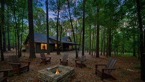 Une cabane dotée d’un foyer en pierre, entourée de fauteuils Adirondack, située dans une zone boisée.