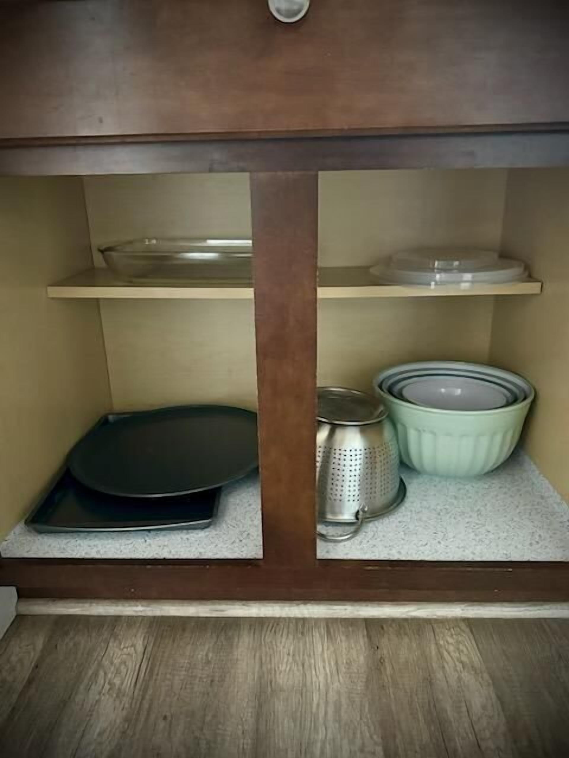 Una cocina con un armario de madera, una bandeja negra para hornear, un colador y un cuenco verde sobre la encimera.
