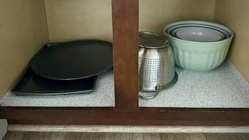 Una cocina con un armario de madera, una bandeja negra para hornear, un colador y un cuenco verde sobre la encimera.