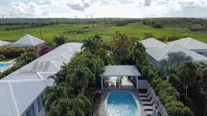 Un resort con varias edificaciones, una piscina y vistas a parques eólicos en la distancia.