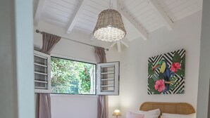 Un dormitorio con cama, lámpara colgante, ventana con cortinas, un cuadro en la pared y una mesita de noche con lámpara.