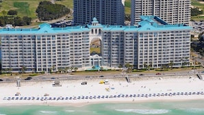 Un gran hotel con una cúpula central y varias alas, ubicado en una playa con una larga hilera de sombrillas.