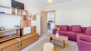 Una sala de estar moderna con un mueble de madera, un televisor de pantalla plana, un sofá rosa y una mesita con un jarrón de flores.