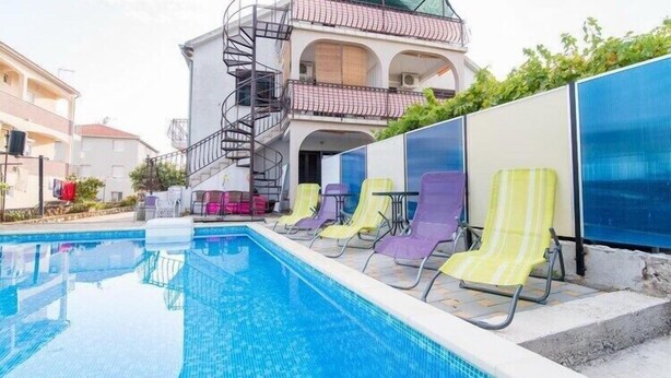 Una piscina con sillas de descanso, una escalera de caracol y un edificio con balcones.