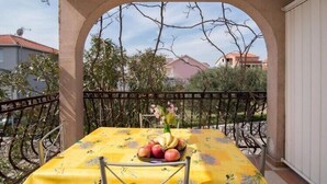A balcony with a table covered by a yellow tablecloth, a fruit basket, and a vase with flowers. - Apartments Fidelis - Two Bedroom Apartment with Terrace and Pool View(5) (Okrug Gornji)