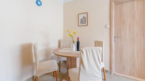 Un coin repas avec une table ronde, quatre chaises, un vase rempli de fleurs jaunes, une bouteille de vin et un tableau encadré accroché au mur.