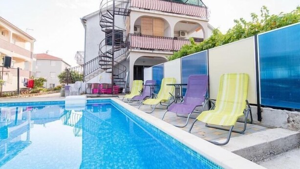 Ein Schwimmbecken mit Liegestühlen und ein Gebäude mit Balkon und Wendeltreppe.