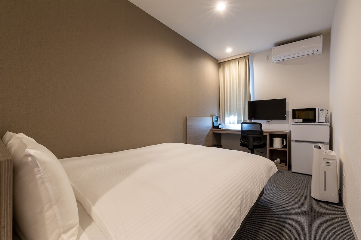 A hotel room with a bed, a desk with a computer, a television, and a microwave.